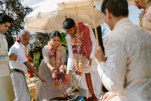 Bride and groom performing traditional Indian wedding ritual in Barcelona under parasol during outdoor ceremony